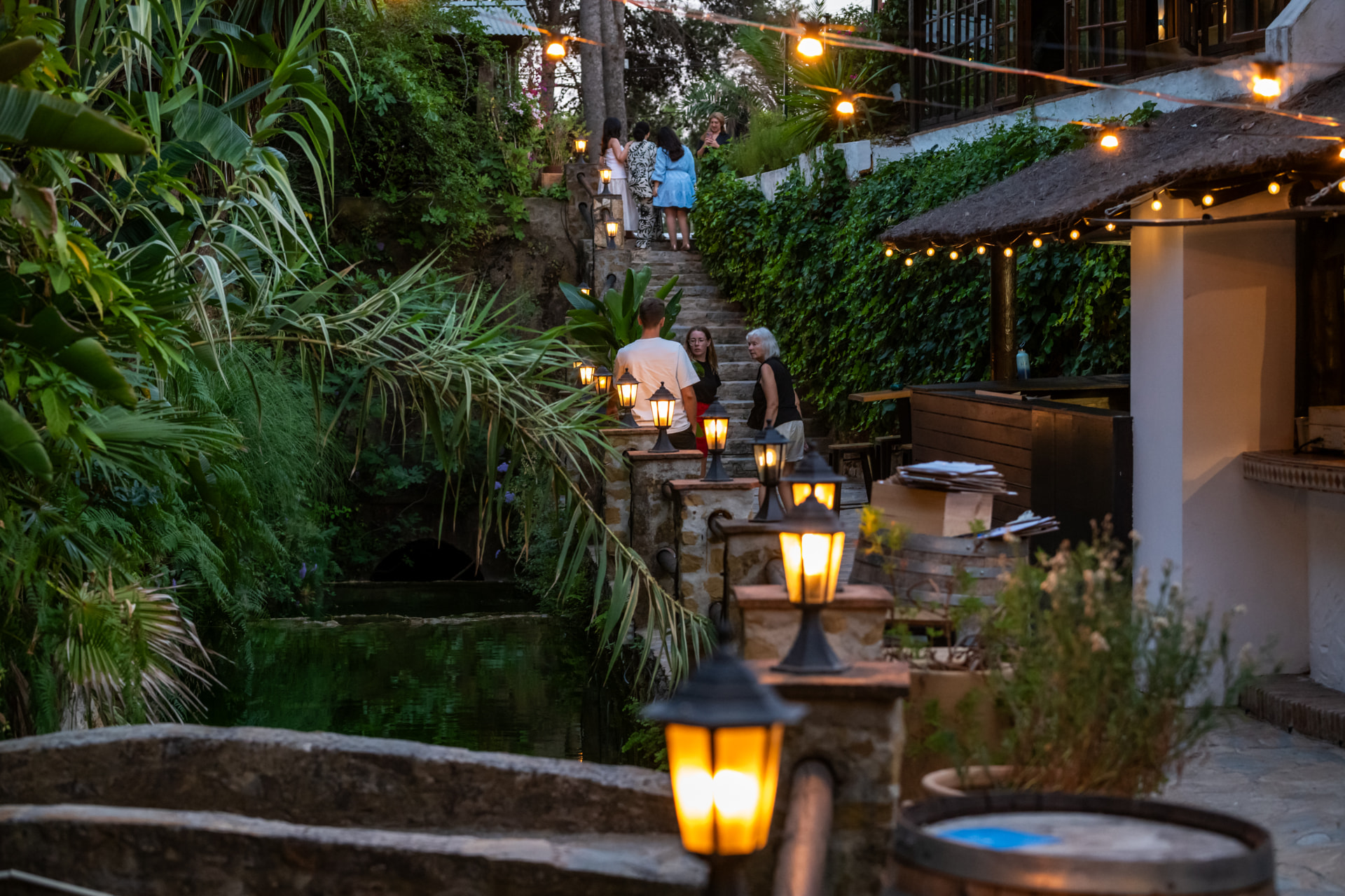 Guests on Le Patio's lantern-lit stone steps beside the river at dusk